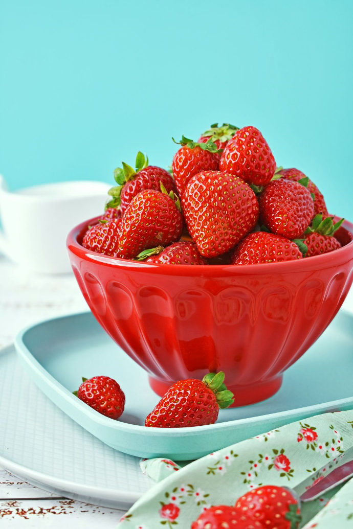 A red bowl filled with strawberries on top of a white plate